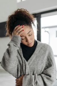 A young woman with a headache and malaise, wearing a cozy sweater indoors.